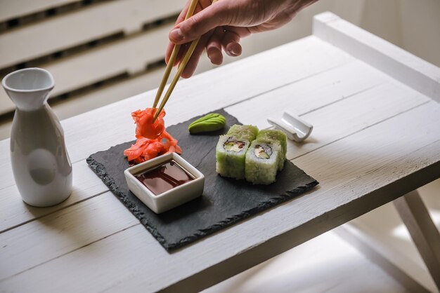 Petits pains traditionnels japonais servis dans un bar à sushis sur tableau blanc. Gros plan sur une main masculine avec un morceau de rouleau