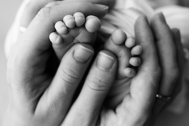 Petits pieds d'un nouveau-né dans les mains de maman La main de paume aimante d'une mère Image conceptuelle de la maternité Gros plan mise au point sélective Photographie professionnelle en noir et blanc