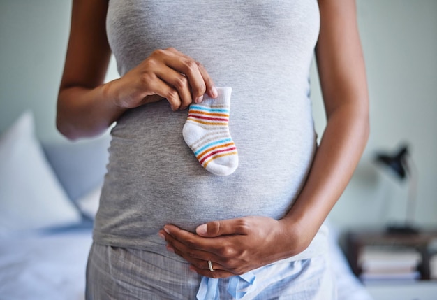 Les petits pieds ont besoin de petites chaussettes Photo recadrée d'une femme enceinte tenant une chaussette de bébé devant son ventre