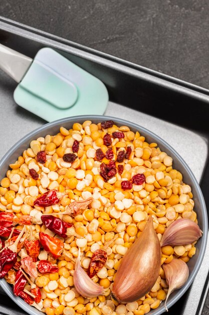 Petits pois assaisonnés dans un bol et une spatule dans une plaque à pâtisserie. Fond noir. Mise à plat