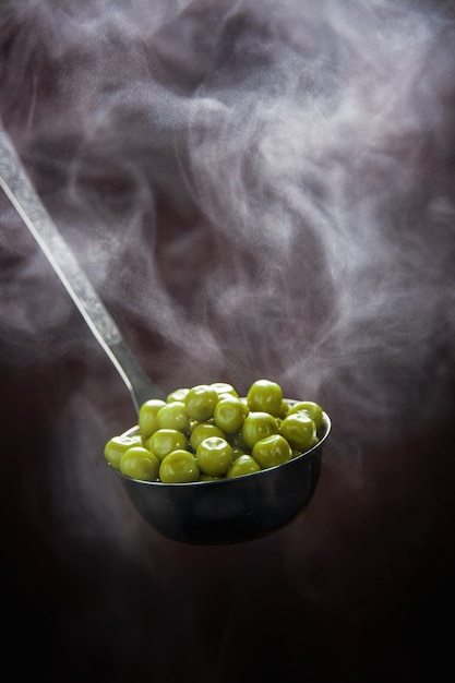 Petits pois verts chauds avec de la vapeur dans la louche.