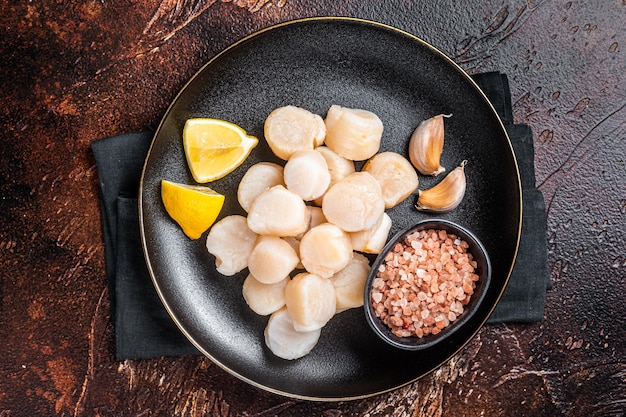 Pétoncles crus fruits de mer sur une assiette avec sel rose et citron Fond sombre Vue de dessus