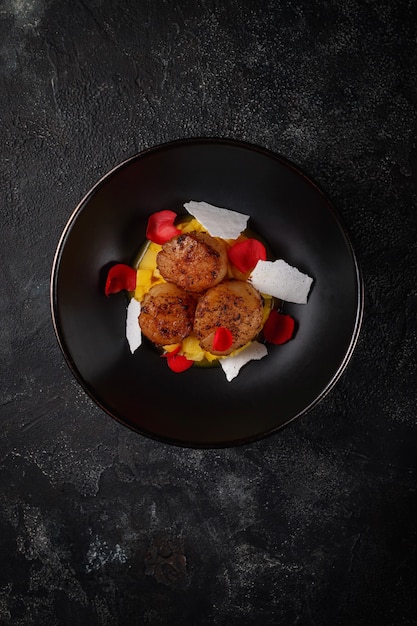 Pétoncles pectinés grillés avec des cubes d'ananas dans une plaque noire sur une table en pierre sombre