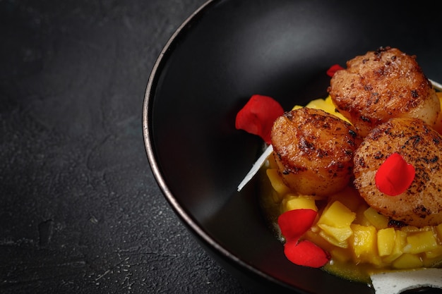 Pétoncles pectinés grillés avec des cubes d'ananas dans une plaque noire sur une table en pierre sombre