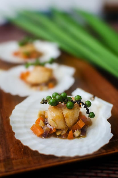 Pétoncles poêlés aux légumes sur une coquille Saint-Jacques.