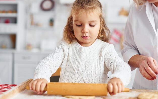 Pétrit la pâte Grand-mère aînée avec sa petite petite-fille prépare des bonbons pour Noël dans la cuisine