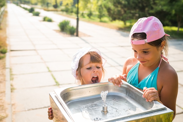 Peu de jolies filles assoiffées boit de l'eau d'un évier dans la rue par une chaude journée d'été ensoleillée