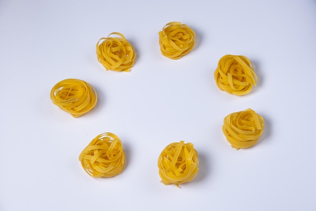 Peu de nids de fettuccine faits maison en forme de cercle isolés sur fond blanc