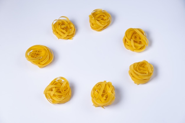 Peu de nids de fettuccine faits maison en forme de cercle isolés sur fond blanc