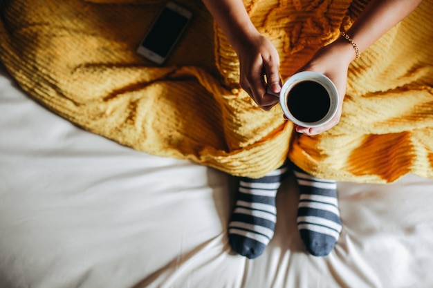 Un peuple portant des chaussettes sous des couvertures sur le lit et tenant une tasse de café