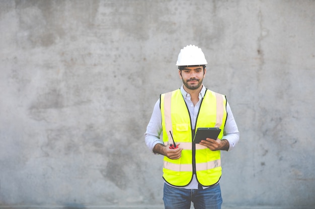 Peuples hispaniques ou moyen-orientaux. Portrait de travailleur de la construction tenant radio rouge et tablette numérique isoler sur fond de ciment gris. Ingénieur de projet sur chantier.