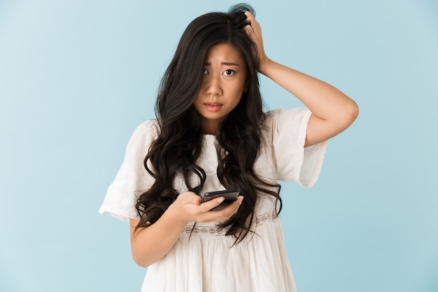 Peur asiatique belle femme isolée sur mur bleu à l'aide de téléphone mobile