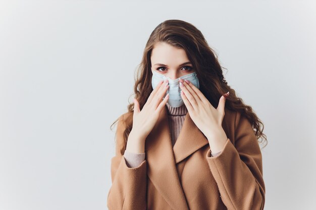 Peur de jeune femme en masque médical debout sur un mur gris.