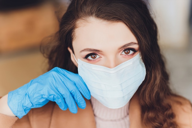 Peur de jeune femme en masque médical debout sur un mur gris.