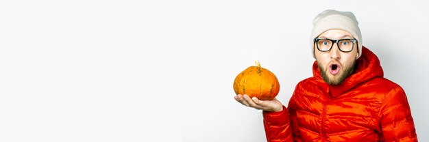 Peur de jeune homme dans une veste rouge, chapeau, tient une citrouille