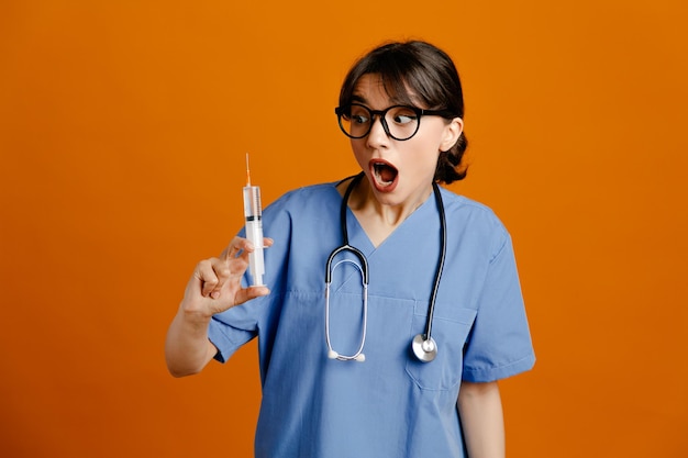 Peur tenant la seringue jeune femme médecin portant un stéthoscope fith uniforme isolé sur fond orange