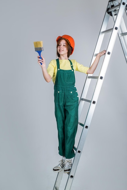 Peut réparer tout enfant constructeur sur chantier ingénieur ingénieur architecte en atelier rénovation et réparation adolescente en casque et combinaison sur escabeau enfant sur échelle porter un casque