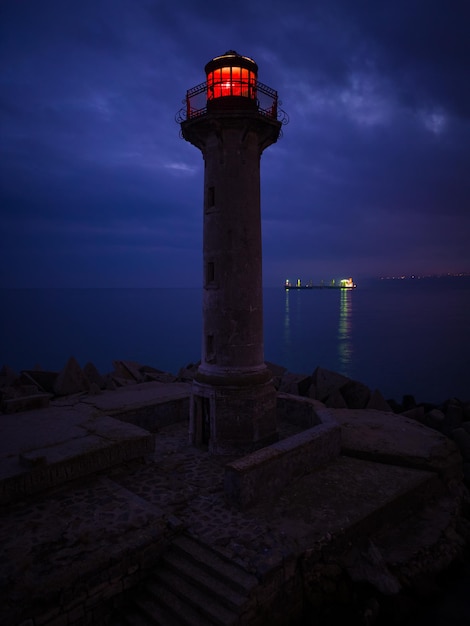 Phare au bord de la mer avec lumière rouge la nuit sur fond de lumières des navires