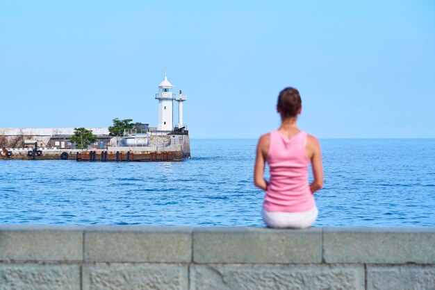 Un phare dans la mer et une fille floue sur la plage.