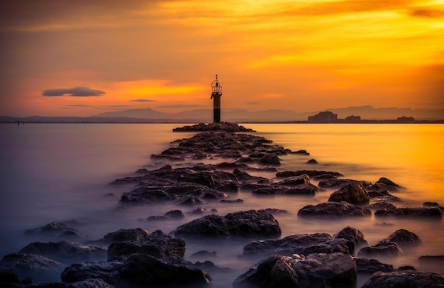 Phare entouré de rochers et de mer avec une longue exposition lors d'un magnifique coucher de soleil doré à Roses