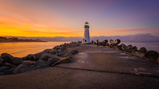 un phare est sur une jetée avec des rochers en arrière-plan