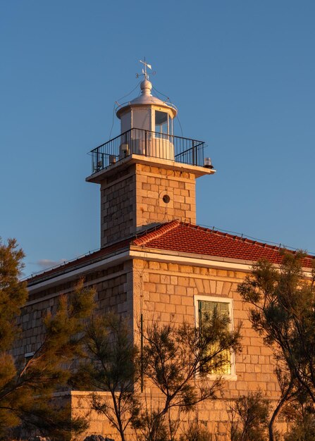 Phare avec une girouette sur le toit contre le ciel bleu