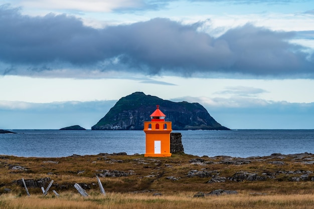 Photo phare orange avec un immense îlot au loin
