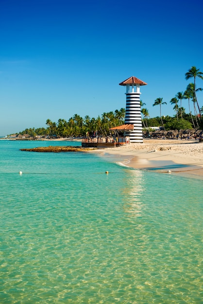 Phare rayé sur le rivage sablonneux avec des palmiers. L'eau claire de la mer des Caraïbes.