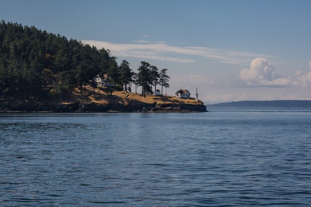 Un phare sur le rivage. Le soleil illumine la forêt, la maison du gardien de phare et le rivage.