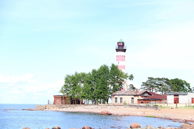 Phare rouge et blanc avec des maisons abandonnées sur les rochers de la plage dans l'eau au premier plan