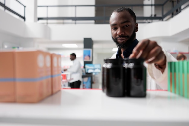 Pharmacien afro-américain prenant des bouteilles de médicaments de l'étagère de la pharmacie, mise au point sélective. Vendeur de pharmacie mettant des paquets de pilules en gros plan, vendant des suppléments, vue de face