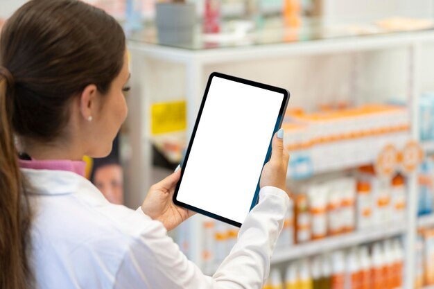 Pharmacien féminin regardant l'écran d'une tablette numérique dans la pharmacie