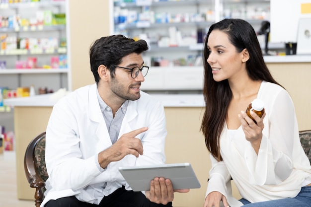 Photo pharmacien masculin du moyen-orient avec tablette numérique vendant des médicaments à une patiente et faisant des recommandations de médicaments en pharmacie moderne