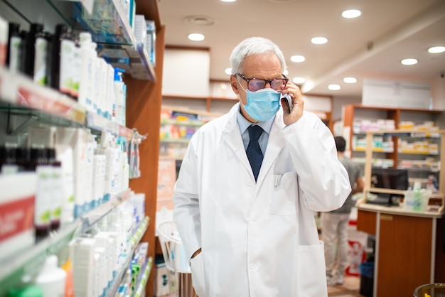 Pharmacien masqué parlant au téléphone en marchant dans sa pharmacie, concept de coronavirus