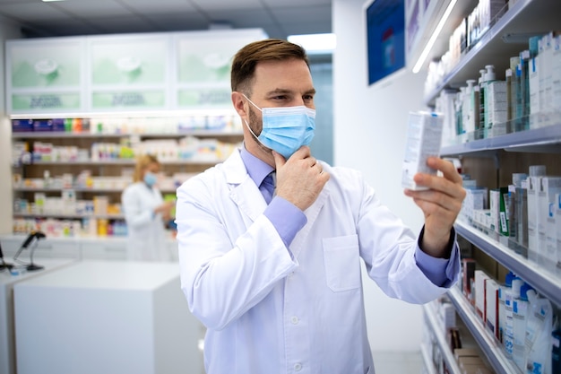 Pharmacien portant un masque et une blouse blanche tenant des médicaments en pharmacie pendant la pandémie de virus corona.