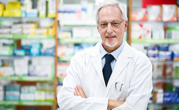 Pharmacien senior souriant et croisant les bras dans son magasin