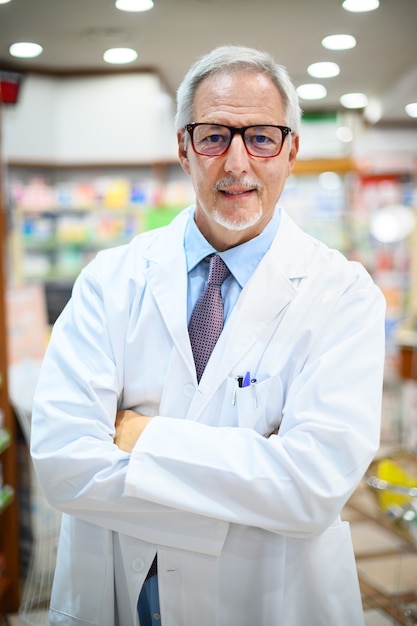 Pharmacien senior souriant et croisant les bras dans son magasin