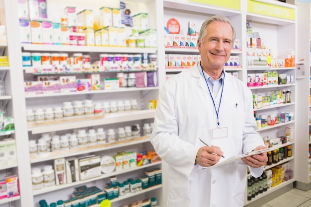 Pharmacien senior souriant écrivant sur le presse-papiers