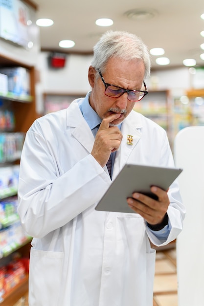Pharmacien senior travaillant sur tablette dans son magasin