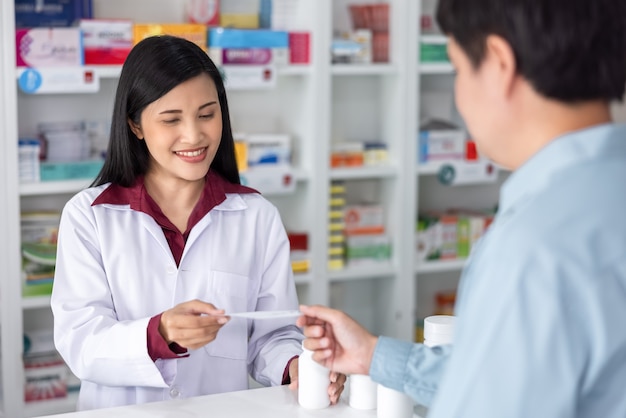 Une pharmacienne asiatique reçoit une liste papier de médicaments de patients masculins dans une pharmacie moderne en Thaïlande