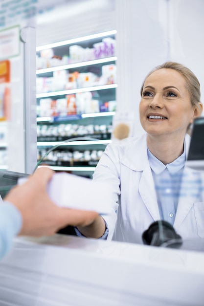 Une pharmacienne assez polie servant un acheteur demande une ordonnance pour un médicament en souriant