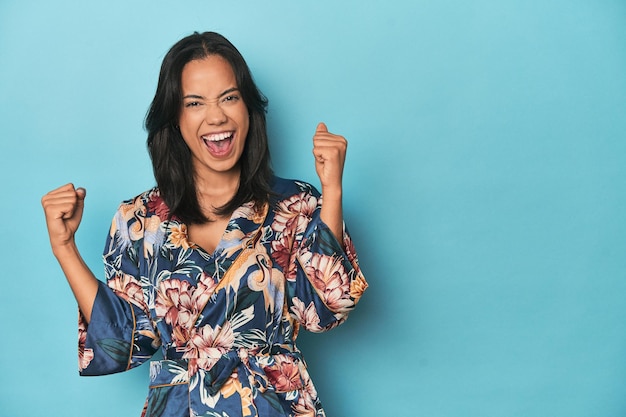 Une Philippine en kimono floral sur un studio bleu soulevant le poing après un concept gagnant de victoire