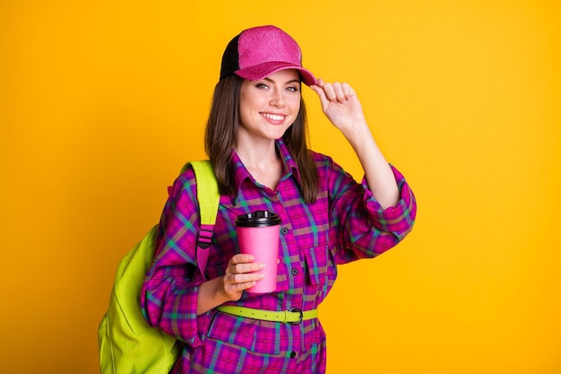 Photo d'une adolescente assez gaie tenir une tasse de chapeaux tactiles aller à l'école porter une chemise rose sac ceinture vert isolé sur fond de couleur jaune