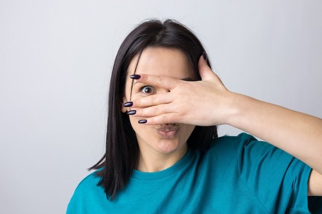 Photo d'une adolescente brune couvrant le visage avec les mains et regardant à travers ses doigts.