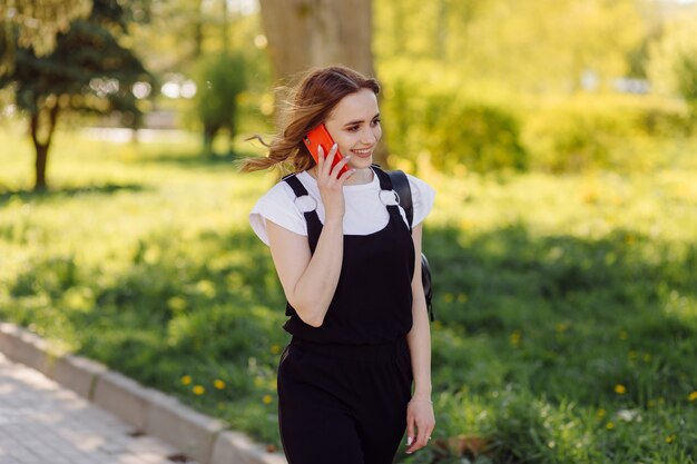 Photo d'une adolescente positive et joyeuse passe du temps dans le parc et utilise un téléphone portable.