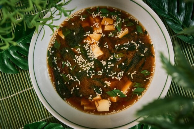 Une photo aérienne d'une assiette de soupe au poulet et aux nouilles prise d'en haut sur une texture rustique sombre avec une cuillère une louche en bois avec des tranches de pain au poivre et une place pour le texte