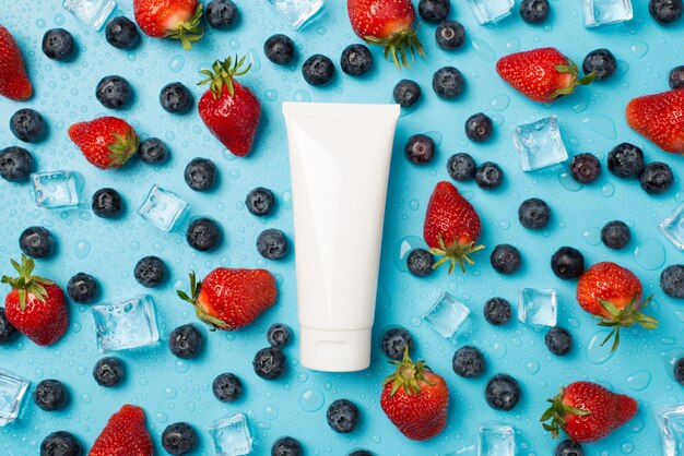 Photo aérienne de bleuets fraises cubes gouttes d'eau glacée et tube blanc de crème isolé sur fond bleu