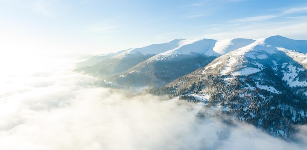 Photo aérienne du lever de soleil majestueux dans les montagnes La vallée entre les montagnes est couverte de brouillard et est éclairée par les rayons chauds du soleil levant Montagnes couvertes de forêt naturelle