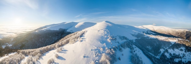 Photo aérienne du lever de soleil majestueux dans les montagnes La vallée entre les montagnes est couverte de brouillard et est éclairée par les rayons chauds du soleil levant Montagnes couvertes de forêt naturelle