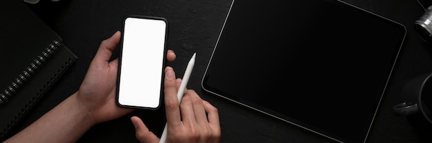 Photo aérienne d'un homme tenant un smartphone à écran blanc dans un espace de travail concept moderne sombre